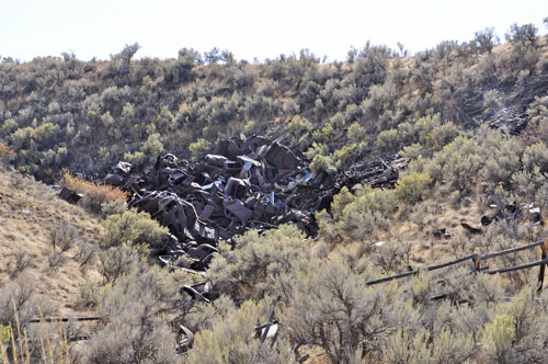 A pile of very old cars in a junk yard area