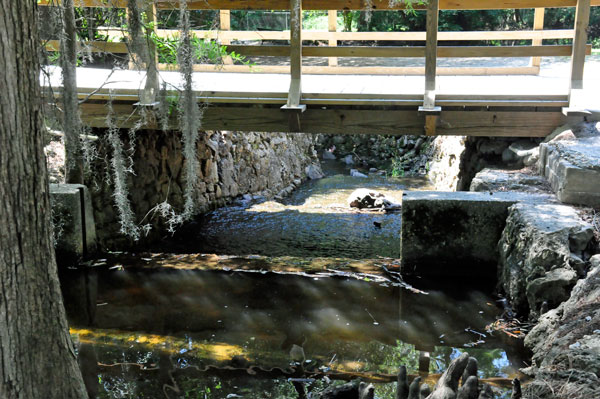 small waterfall under a walk bridge