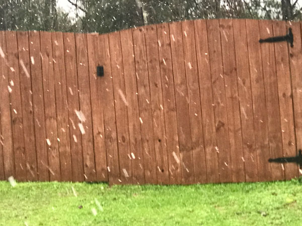 Snow falling near the fence.