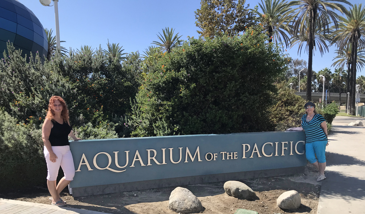 Karen Duquette and her sister at the Aquarium of the Pacific sign